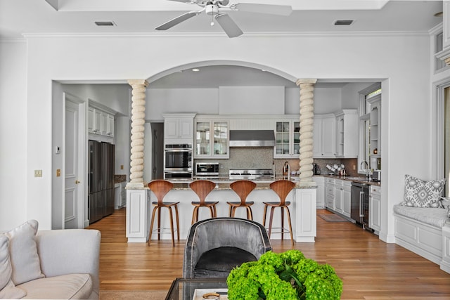 kitchen with wall chimney exhaust hood, sink, a kitchen breakfast bar, stainless steel appliances, and white cabinets