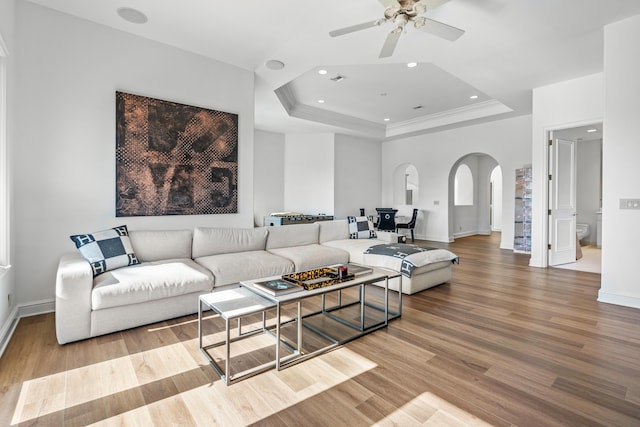 living room featuring ornamental molding, light hardwood / wood-style flooring, ceiling fan, and a tray ceiling