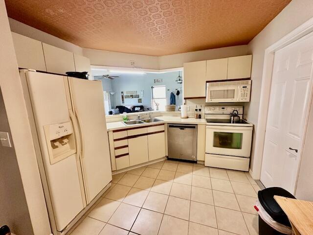 kitchen featuring white appliances, sink, a textured ceiling, and light tile patterned floors