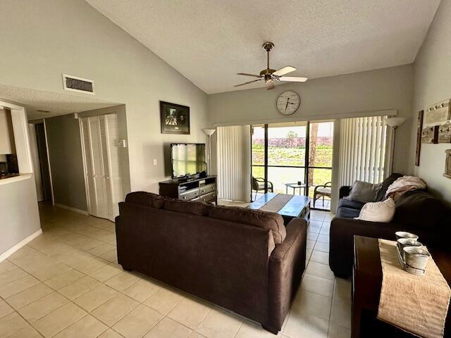 tiled living room with ceiling fan, high vaulted ceiling, and a textured ceiling