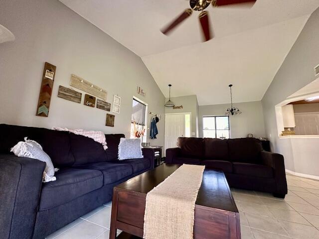 living room featuring light tile patterned floors, ceiling fan with notable chandelier, and high vaulted ceiling