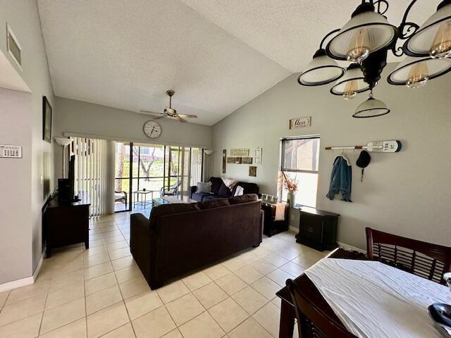 living room with light tile patterned flooring, ceiling fan, vaulted ceiling, and a textured ceiling