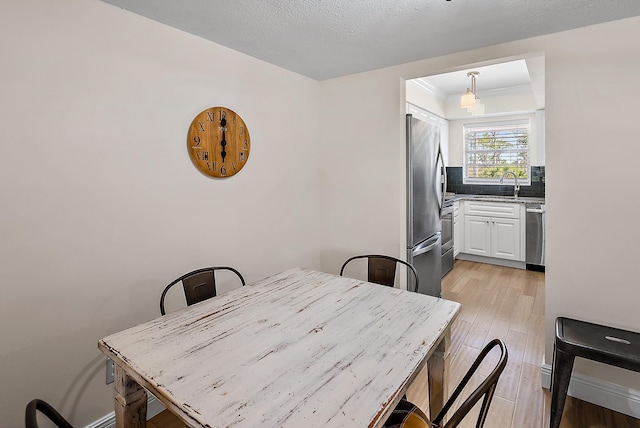 dining room featuring sink, a textured ceiling, and light wood-type flooring