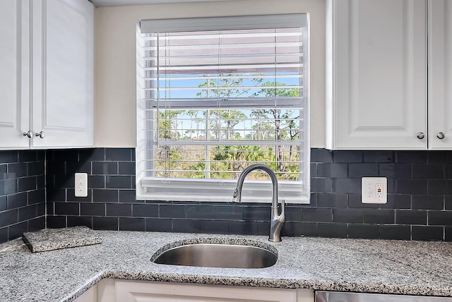 kitchen featuring white cabinetry, sink, backsplash, and light stone counters