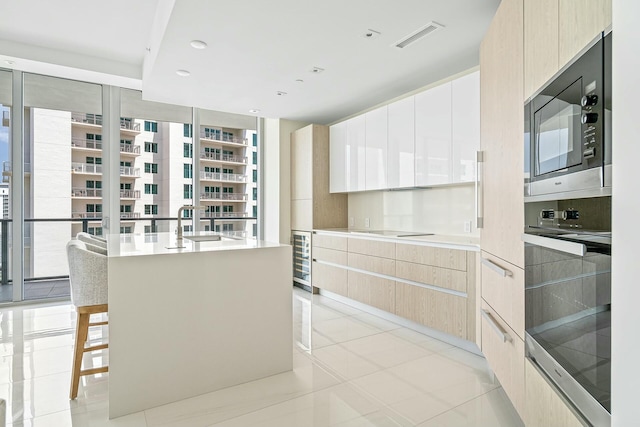 kitchen with built in microwave, a breakfast bar, a center island with sink, oven, and white cabinets