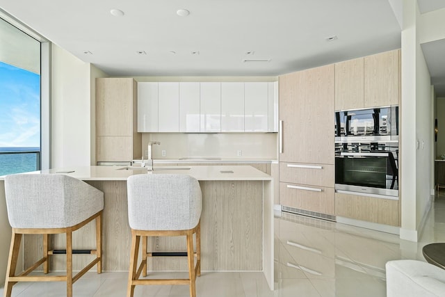 kitchen featuring built in microwave, a water view, white cabinetry, a center island with sink, and oven