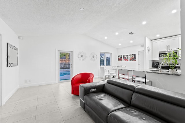 living room with light tile patterned floors, vaulted ceiling, sink, and a textured ceiling