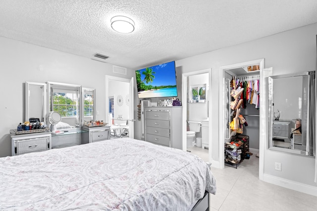 bedroom with ensuite bathroom, a spacious closet, light tile patterned floors, a textured ceiling, and a closet