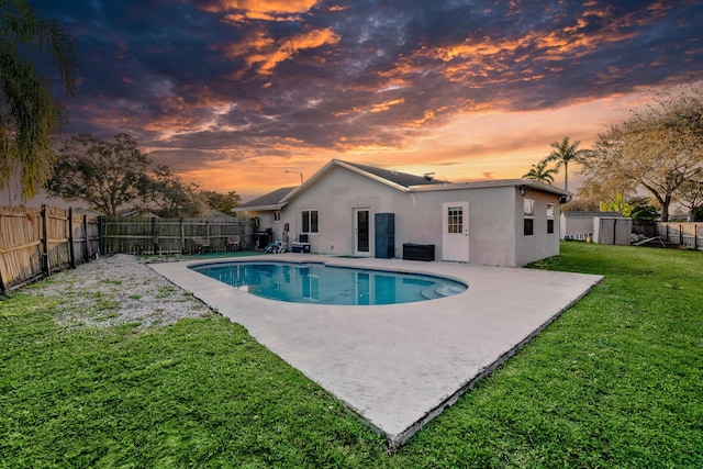 pool at dusk featuring a patio and a lawn