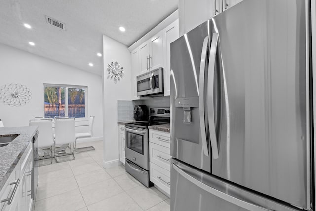 kitchen featuring stone counters, appliances with stainless steel finishes, white cabinets, decorative backsplash, and light tile patterned floors