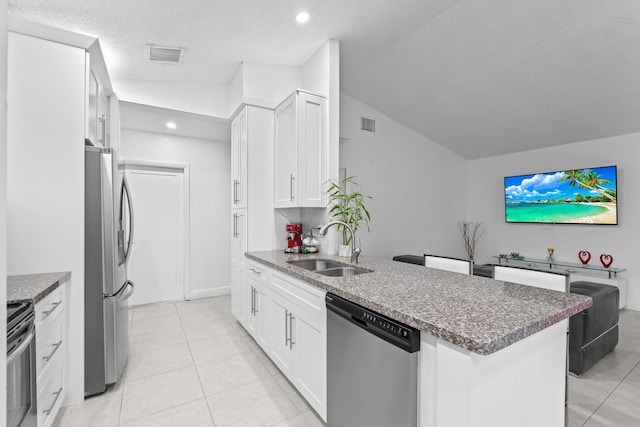 kitchen with sink, white cabinetry, vaulted ceiling, light tile patterned floors, and stainless steel appliances