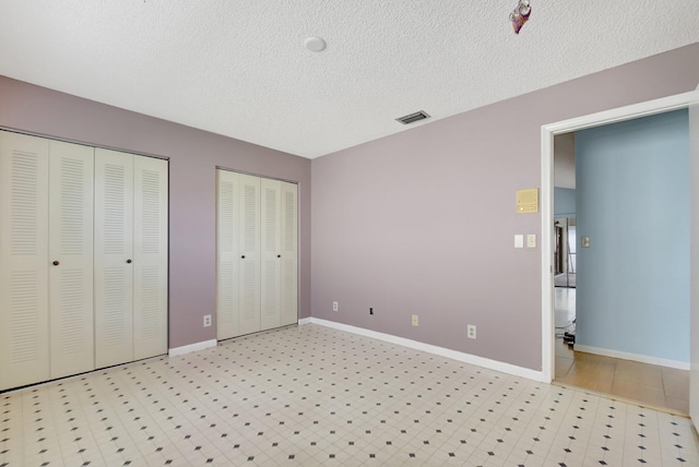 unfurnished bedroom with two closets and a textured ceiling