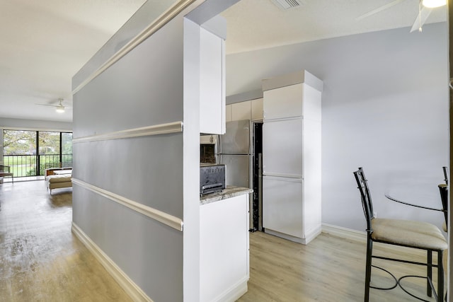 interior space with white cabinetry, light stone counters, light hardwood / wood-style flooring, and ceiling fan