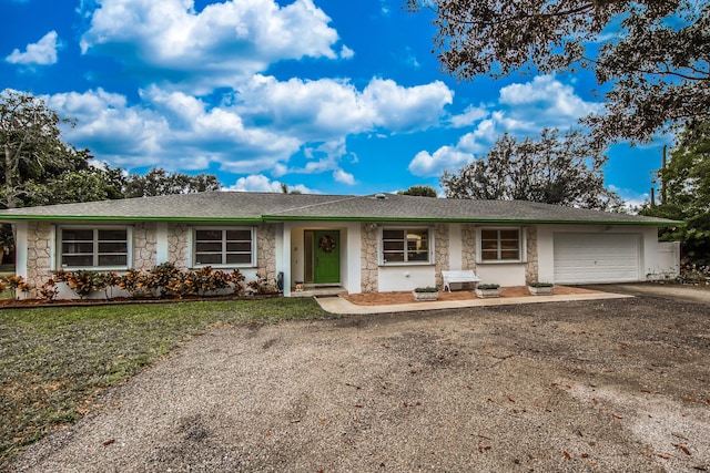 ranch-style house with a garage, stone siding, driveway, roof with shingles, and a front yard