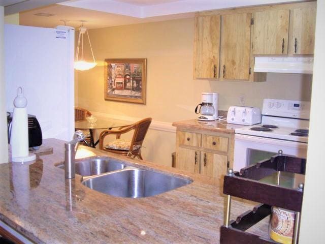 kitchen featuring light brown cabinetry, sink, light stone counters, hanging light fixtures, and white range with electric stovetop