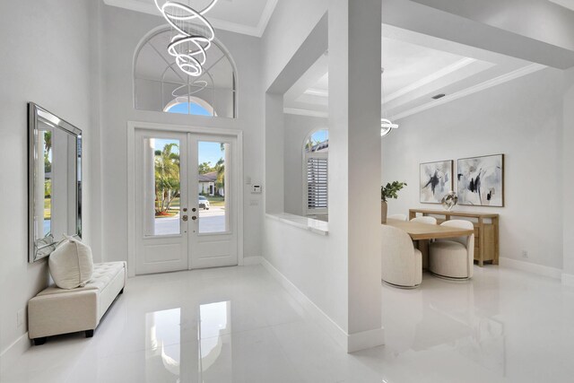 entryway featuring a notable chandelier, a towering ceiling, a raised ceiling, french doors, and ornamental molding