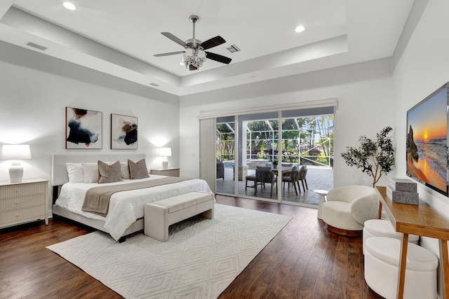 bedroom with a tray ceiling, access to exterior, dark hardwood / wood-style floors, and ceiling fan