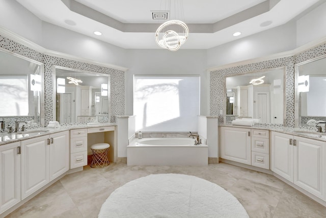 bathroom featuring a raised ceiling, a washtub, a notable chandelier, and vanity