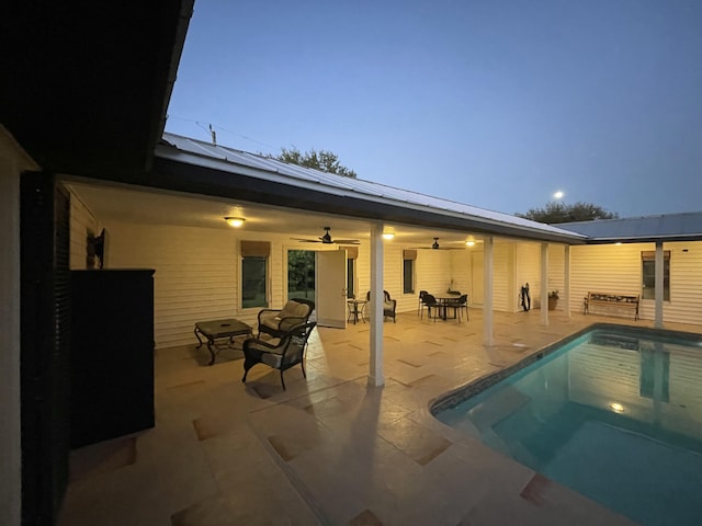 pool at dusk with ceiling fan and a patio area