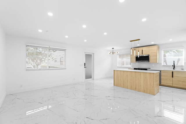 kitchen featuring light brown cabinetry, sink, decorative light fixtures, a kitchen island, and a notable chandelier