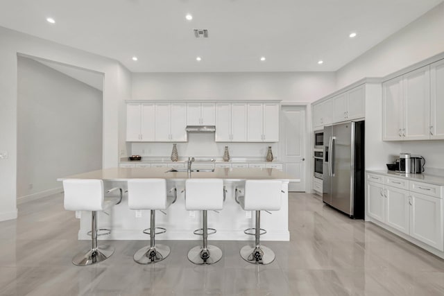 kitchen with stainless steel appliances, white cabinets, and a center island with sink