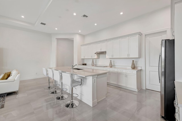 kitchen with stainless steel refrigerator, white cabinetry, a kitchen island with sink, a kitchen breakfast bar, and black electric cooktop