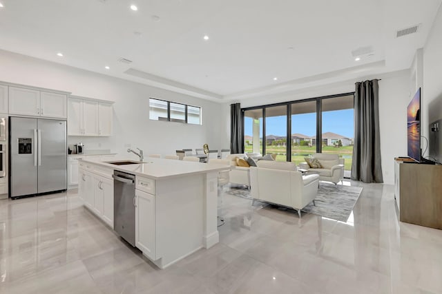 kitchen featuring a kitchen island with sink, a tray ceiling, white cabinets, and appliances with stainless steel finishes