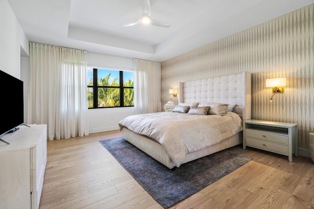 bedroom with light hardwood / wood-style flooring, ceiling fan, and a tray ceiling