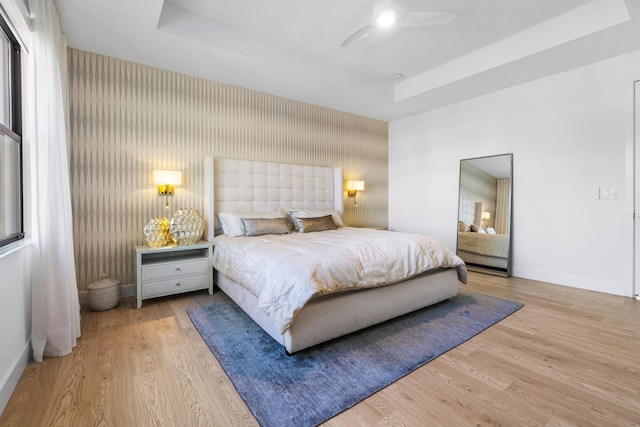 bedroom with a tray ceiling, ceiling fan, and light wood-type flooring