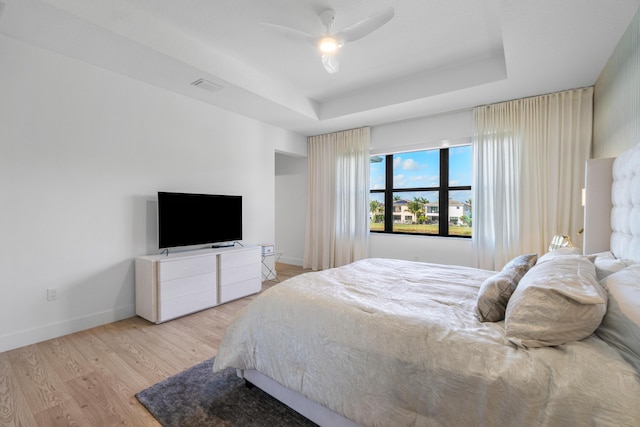 bedroom with ceiling fan, a tray ceiling, and light wood-type flooring