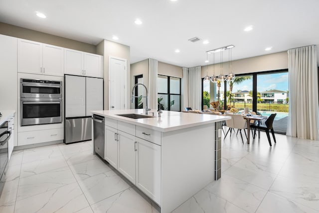 kitchen with sink, decorative light fixtures, a kitchen island with sink, and white cabinets