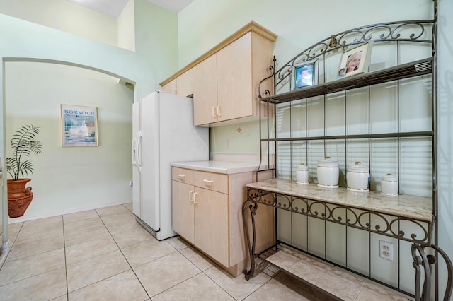 kitchen featuring white fridge with ice dispenser, light tile patterned floors, and light brown cabinets