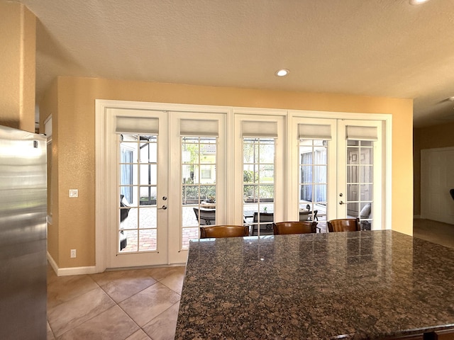 interior space with a textured ceiling, recessed lighting, french doors, light tile patterned floors, and baseboards