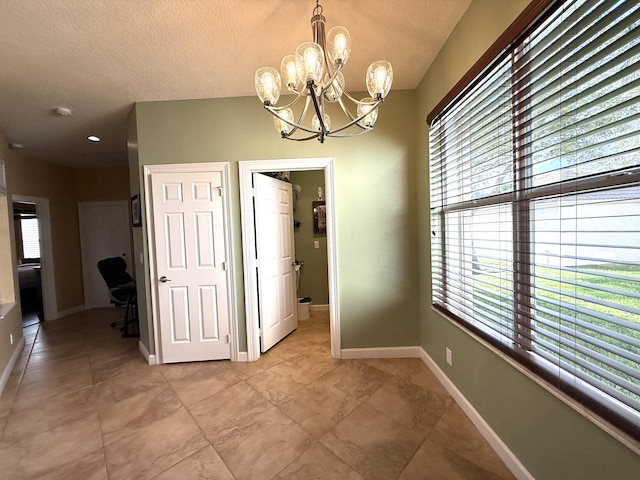 unfurnished dining area featuring baseboards, a textured ceiling, and a chandelier