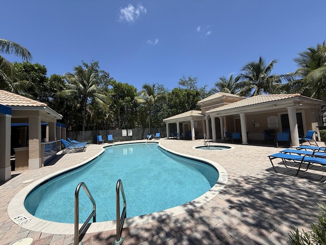 community pool with a patio area, a hot tub, and fence