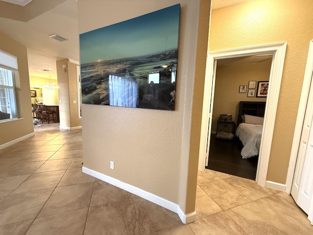 corridor featuring tile patterned floors, visible vents, baseboards, and an inviting chandelier