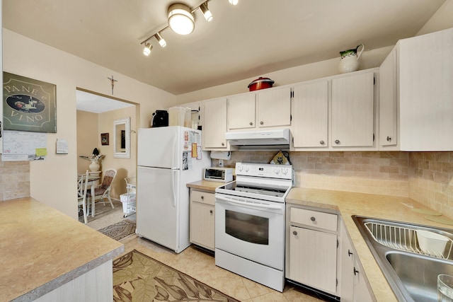 kitchen with tasteful backsplash, under cabinet range hood, light countertops, white appliances, and a sink