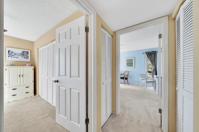 hall featuring light colored carpet and a textured ceiling