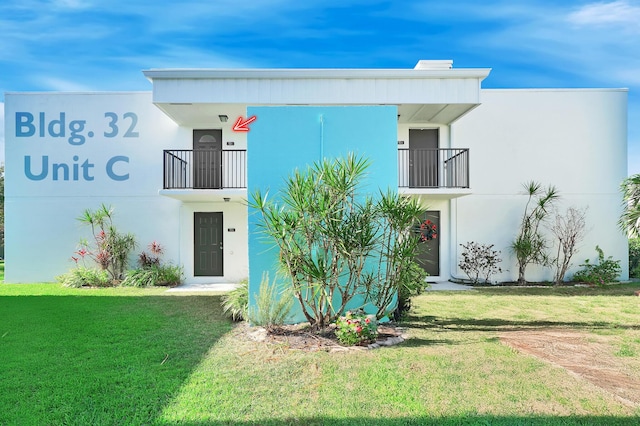 view of front facade featuring stucco siding, a balcony, and a front lawn