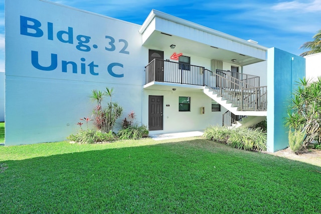 back of property with stairs, a lawn, and stucco siding