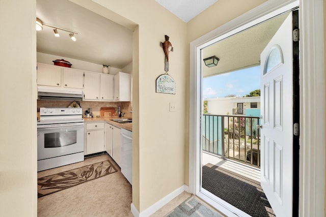 kitchen featuring under cabinet range hood, light countertops, decorative backsplash, white appliances, and white cabinetry