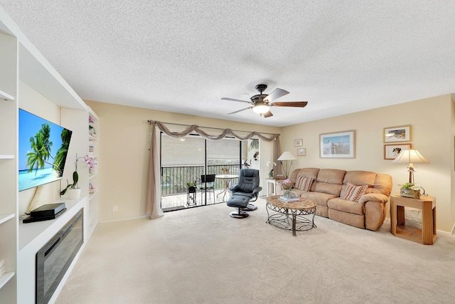 carpeted living area featuring a glass covered fireplace, a textured ceiling, and a ceiling fan