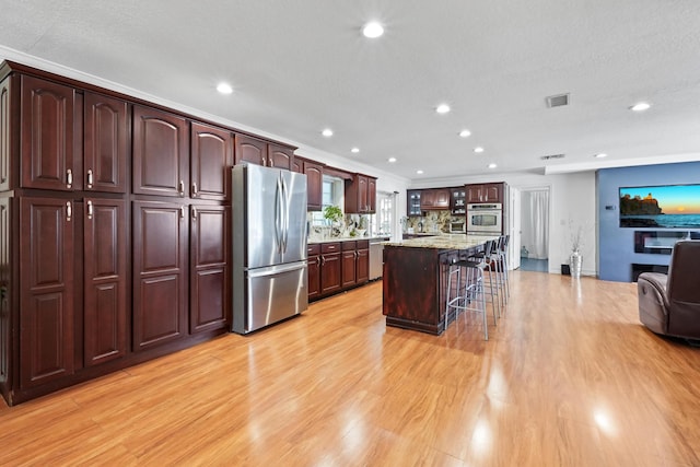 kitchen with a breakfast bar, stainless steel appliances, light stone countertops, a kitchen island, and light wood-type flooring