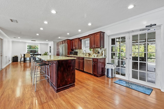 kitchen featuring a kitchen bar, sink, appliances with stainless steel finishes, a kitchen island, and light stone countertops