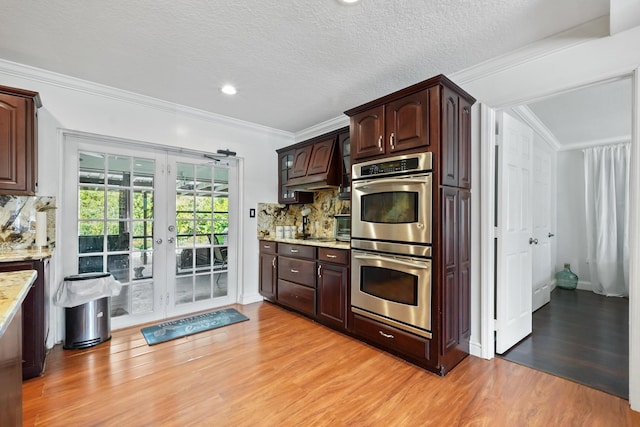 kitchen with double oven, backsplash, crown molding, dark brown cabinets, and light wood-type flooring