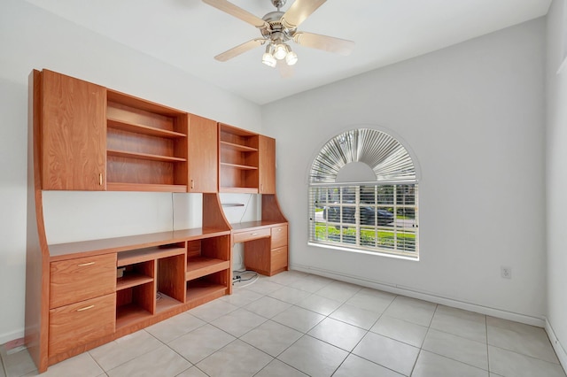 unfurnished office featuring light tile patterned flooring, ceiling fan, and built in desk