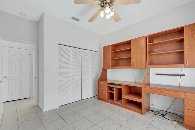 unfurnished office featuring light tile patterned floors, built in desk, and ceiling fan