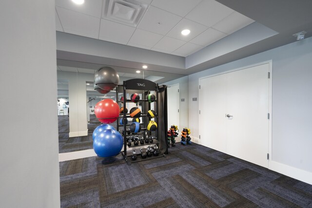 workout area with a paneled ceiling, elevator, and dark colored carpet