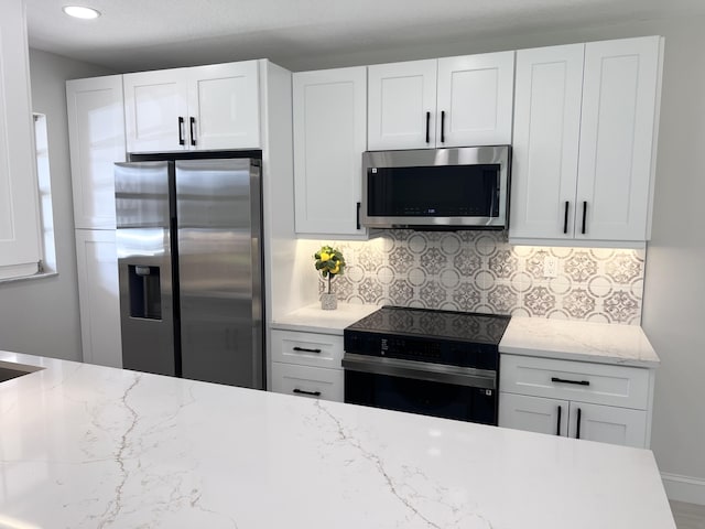 kitchen featuring stainless steel appliances, light stone counters, white cabinets, and backsplash