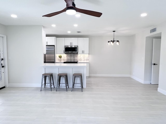 kitchen featuring a breakfast bar area, appliances with stainless steel finishes, white cabinetry, hanging light fixtures, and tasteful backsplash